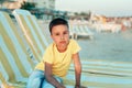 boy in yellow t-shirtsitting on bench near sea alone on beach at sunset. Happy family travel. Summer vacation with child