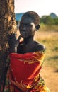 BOYA TRIBE, SOUTH SUDAN - MARCH 10, 2020: Young woman in colorful garment touching lip and looking away while leaning on Royalty Free Stock Photo