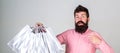 Boyfriend carrying lots of shopping bags and pointing at bags. Man with beard carries bunch of shopping bags, grey Royalty Free Stock Photo