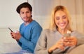 Boyfriend Catching Girlfriend Chatting With Lover Sitting On Sofa Indoor