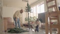 Couple in a homewear setting up an artificial Christmas tree and playing with a dog. Full shot high-quality image. Royalty Free Stock Photo