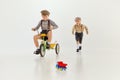 Boys, childred in retro clothes riding vintage bicycle, running over grey studio background. Concept of game, childhood Royalty Free Stock Photo