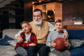 Boys on couch with their grandfather cheering for a basketball game and holding a basketball ball. Huge sports fanats.