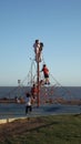 A group of children play climbing between the rope net. Climbing up to the sky with the sea in the background. Boys and girls alik