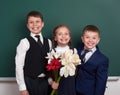 Boys giving girl flowers, elementary school child near blank chalkboard background, dressed in classic black suit, group pupil, ed