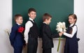 Boys giving girl flowers, elementary school child near blank chalkboard background, dressed in classic black suit, group pupil, ed