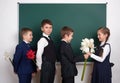 Boys giving girl flowers, elementary school child near blank chalkboard background, dressed in classic black suit, group pupil, ed