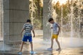 Boys Jumping In Water Fountains. Children Playing With A City Fountain On Hot Summer Day. Happy Friends Having Fun In Fountain.