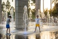 Boys jumping in water fountains. Children playing with a city fountain on hot summer day. Happy friends having fun in fountain. Royalty Free Stock Photo