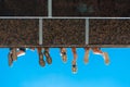 Boys legs in shoes hanging from the bridge against blue sky