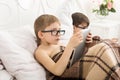 Two boys play at laptop and tablet with dog in bed Royalty Free Stock Photo