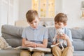 Boys are reading book while sitting on couch at home. Brothers read book. Older Royalty Free Stock Photo