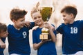 Boys sports team celebrating victory. Happy children holding golden trophy. Kids football team raising winners` cup. Youth sport