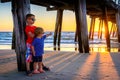 Boys standing on the beach under pier at sunset Royalty Free Stock Photo