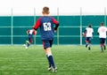 Boys in white and blue sportswear plays football on field, dribbles ball. Young soccer players with ball on green grass. Royalty Free Stock Photo