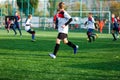 Boys in white and blue sportswear plays football on field, dribbles ball. Young soccer players with ball on green grass.