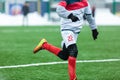 Boys in white sportswear running on a soccer field with snow in the background.