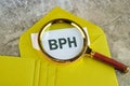 BPH Benign Prostatic Hyperplasia. BPH written through a magnifying glass on a piece of mustard-colored envelope Royalty Free Stock Photo