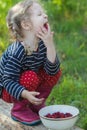 Braided blonde little girl bringing hand to mouth and enjoying of eating ripe garden raspberries