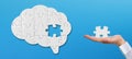 Brain shaped white jigsaw puzzle on blue background. Hand holding a missing piece of the brain puzzle. Royalty Free Stock Photo