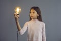 Serious preteen casual girl student looking at glowing lightbulb lamp in hand