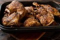 Braised chicken legs in a rosting pan on dark wooden background.