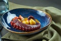 Braised octopus tentacle with tomatoes in a creamy sauce in blue bowl on wooden background. Delicious and luxury seafood. Close up
