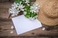 A branch of a blooming apple tree with white flowers, a sheet of paper and a straw hat on a wooden background, with a copy space Royalty Free Stock Photo