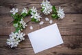 A branch of a blooming apple tree with white flowers and a sheet of paper on a wooden background, with a copy space Royalty Free Stock Photo