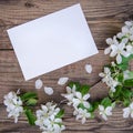 A branch of a blooming apple tree with white flowers and a sheet of paper on a wooden background, with a copy space Royalty Free Stock Photo