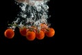 The branch of cherry tomatoes in water splash with bubbles on a black background. Royalty Free Stock Photo