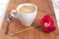 Branch of mallow red flower and white cup of hot coffee with foam with silver spoon on table on wood background closeup Royalty Free Stock Photo