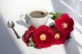 Branch of mallow red flowers and white cup of black coffee with foam, silver teaspoon in the morning sunlight on table Royalty Free Stock Photo