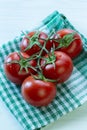 Branch of red tomatoes with water drops on checkered napkin. Bright ripe clean tomatoes branch on green napkin, delicious