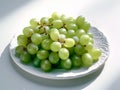 Branch of ripe green grape on a ceramic plate. Juicy lush grapes over white background, closeup shot Royalty Free Stock Photo