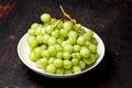 Branch of ripe green grape on plate with water drops. Juicy grapes on wooden background, closeup Royalty Free Stock Photo