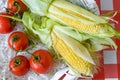 Branch of tomatoes and two cobs of sweet corn in white wooden basket with straw