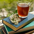 Branches of blooming bird cherry tree and a glass cup with tea on a stack of books by the window. Close up. Royalty Free Stock Photo