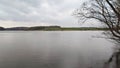 The branches of trees growing on the shore bent over the water of the lake. On the opposite bank there is a green meadow and a for Royalty Free Stock Photo