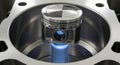 A brand new piston sits inside a cylinder of an engine block reflecting blue light showing precision engineering and automotive Royalty Free Stock Photo