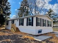 Brand new prefab mobile home with for sale yard sign post, colorful fall foliage near Rochester, New York