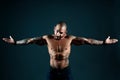 Brash muscular Latino or Cuban with tattoos on his body poses in studio against dark background.