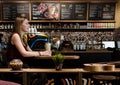 BRASOV, ROMANIA - 26 April 2017: Side of young blonde woman smiling sit at a table in local cafe shop drink frappe