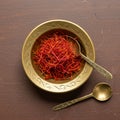 A brass bowl containing saffron threads (Crocus sativus) rests on a wooden surface. Royalty Free Stock Photo