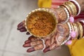 Brass bowl of turmeric paste on palm of indian bride