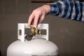 Man opens the valve knob on the top of a propane bottle