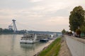 View of the Danube River with pleasure boats, people walking along the embankment and the futuristic bridge.