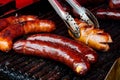 Bratwurst sausages on cast iron griddle. Metal tongs. Royalty Free Stock Photo