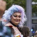 Older drag queen with a wig of blue and purple hair smiles at CSD parade