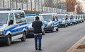 Rear view of a press photographer who is photographing a row of blue and white German police vans with blue light of the Mercedes